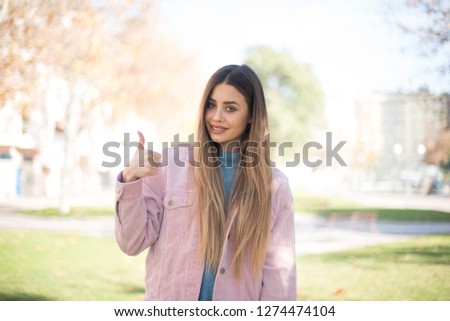 Good job! Portrait of a happy smiling blue eyed young successful woman giving thumb up gesture standing outdoors. Positive human emotion facial expression body language. Funny girl
