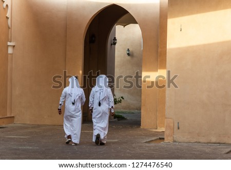 Two unidentifiable Arabic men in white thobe clothing walking away in Doha, Qatar. Royalty-Free Stock Photo #1274476540
