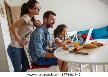 Family breakfast.Young parents with they daughter sitting at the table and watching cartoons on laptop.