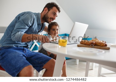 Family breakfast.Father with his daughter sitting at the table and watching cartoons on laptop.