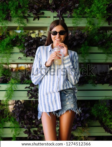 Beautiful young woman with plastic cup of fresh cocktail on green wall background