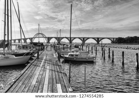 black and white panoramic view of the famous bridge of Moen in Denmark with the marina of Kalvehave in the foreground and a wooden pier leading the view into the picture