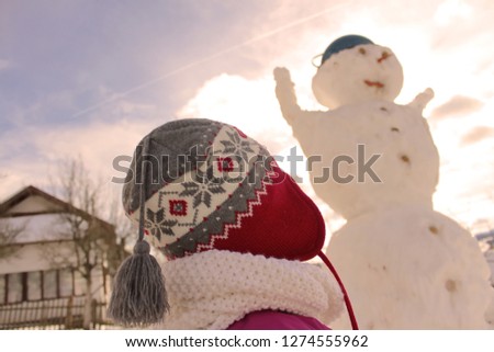 a cute three year old girl with a red cap is making a snowman