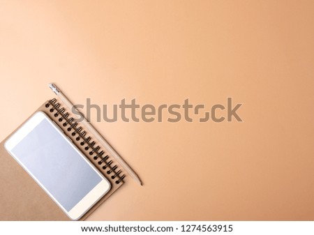 The notebook, pencil, smartphone on color orange background. Flat lay top view.