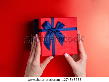 Red box gift with blue ribbon in hand on red background, top view fashion flat lay