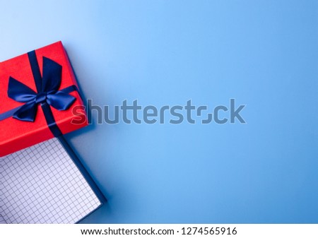 Red box gift with blue ribbon on blue background, top view fashion flat lay