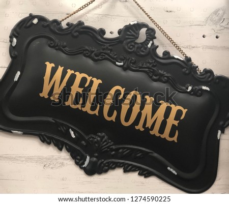 Black and gold welcome sign hanging on exterior wall