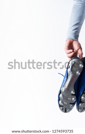Football soccer player holding football boots cleats in hand on white background with copy space.