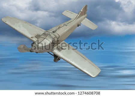 Picture of a retro gray metal toy airplane. In the background, blue sky with clouds and sea.