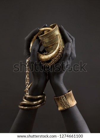 Black woman's hands with gold jewelry. Oriental Bracelets on a black painted hand. Gold Jewelry and luxury accessories on black background closeup. High Fashion art concept  Royalty-Free Stock Photo #1274661100