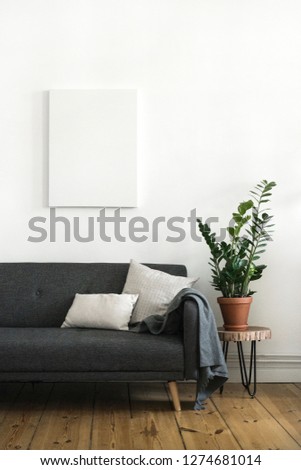 Interior poster painting mock up with empty canvas hanging on white wall, room with sofa and green plant. Interior design photography with copy space