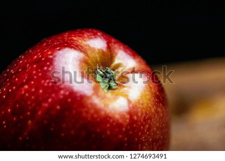 Close up picture of an juicy red apple in dark background, dramatic light, wooden vintage board.