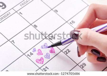 Young girl hand drawing and coloring heart shape in calendar for Valentines day with felt pen. Love and Valentine day holiday concept. Close up, selective focus