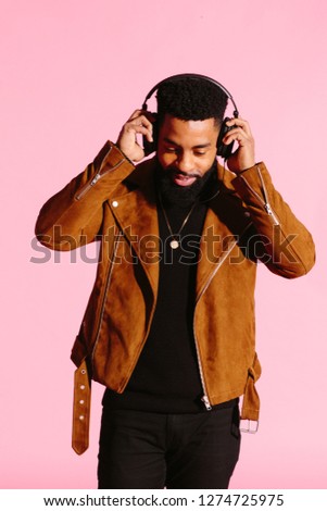 Portrait of a smiling man with beard and headphones, looking down listening to music, isolated on pink studio background