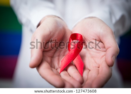Man in shirt holding red aids ribbon on rainbow background Royalty-Free Stock Photo #127473608