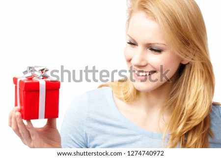 A beautiful young blond woman smiling, holding and looking at a red gift box with a silver bow, isolated on white.