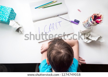School aged boy sitting at the table, frustrated, helpless and sad with himself and his writing because of dysgraphia, shot from above, horizontal position. Royalty-Free Stock Photo #1274749018