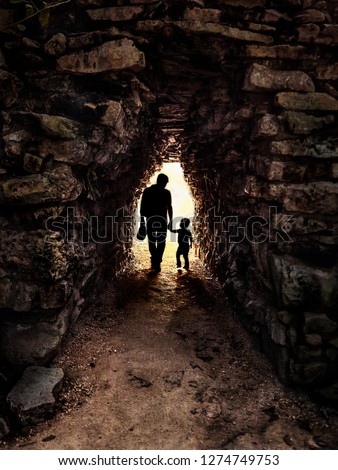 Silhouette of father and son in backlight in a small and dark stone tunnel: Image taken at Tulum in Mexico. Royalty-Free Stock Photo #1274749753