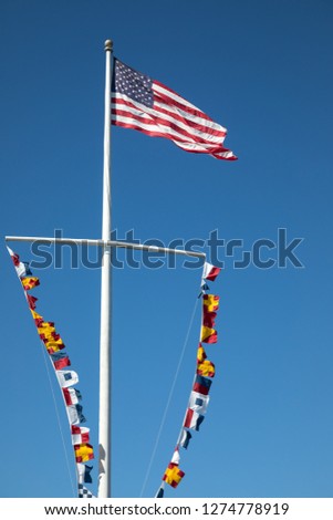 Flag pole with an American flag above nautical flags blowing in the wind, with a blue sky background