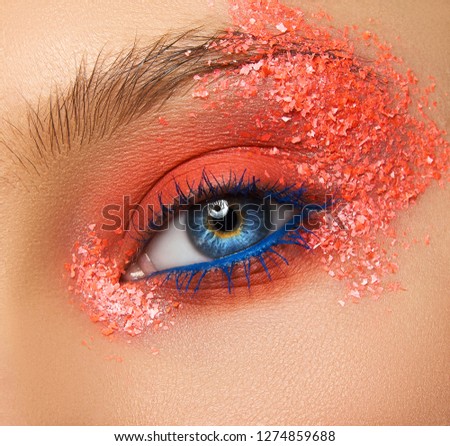 Macro and close-up creative make-up theme: Beautiful female eye with orange sparkles and blue shadows