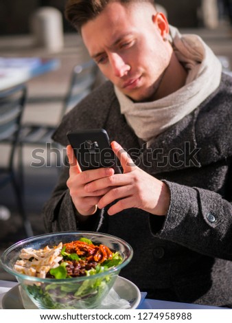 Side view of a handsome young man taking a photo of his food in the restaurant outside