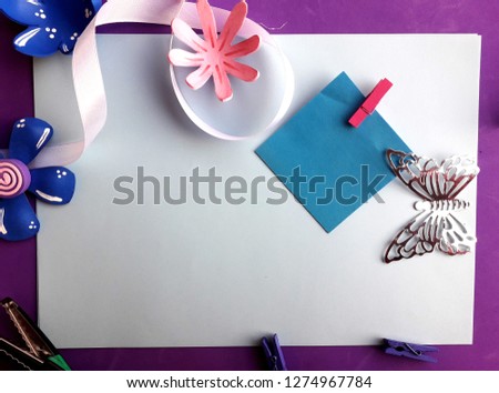 a blue paper with clothespin, some flowers, ribbons and a butterfly on white and purple background