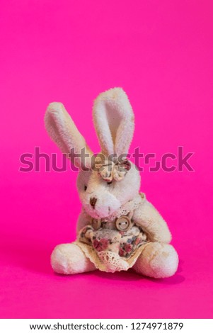 Toy white cartoon rabbit sits on a pink background close up