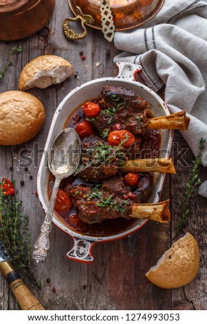 Lamb shanks in rich tomato sauce with bread and herbs, top view
