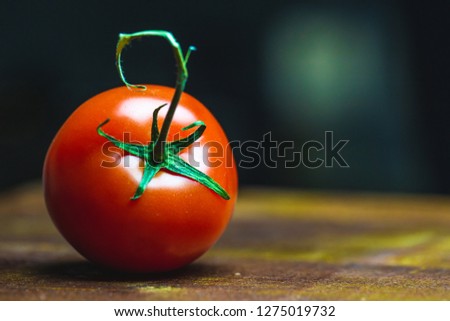 Close up picture of Tomato on old vintage  wooden board. Dark black background, dramatic light. Saturated red tomato.