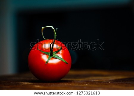 Close up picture of Tomato on old vintage  wooden board. Dark black background, dramatic light. Saturated red tomato.