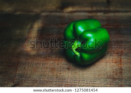 Close up picture of green sweet peper on old vintage brown wooden board, dark black background, dramatic lighting
