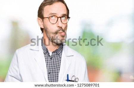 Middle age doctor men wearing medical coat making fish face with lips, crazy and comical gesture. Funny expression.