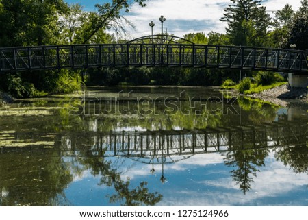 Landscape view of river scene featuring steel bridge, sky reflections on the water and aquatic vegetation