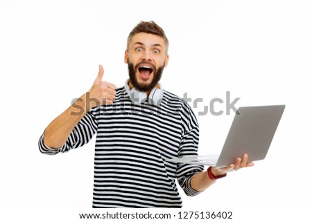 Everything works great. Delighted joyful man holding his laptop while showing a thumbs up gesture