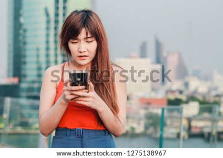A beautiful asian woman reading a message containing bad, terrifying news in smart phone with feeling frightened over city background