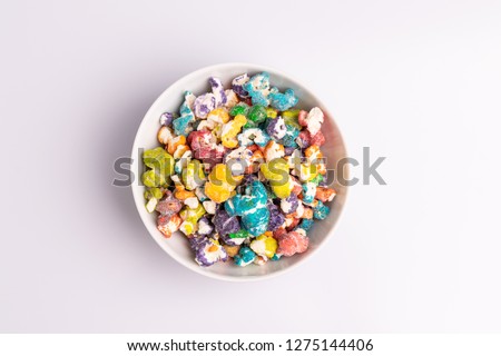 Colored Popcorn candy in white bowl, isolated on white background, soft light, studio shot, copy space. Junk food, fruit flavored popcorn. Colorful, multicolor, candy coated popcorn, top view