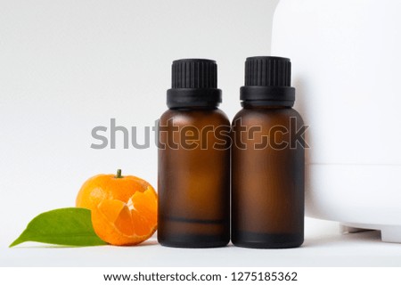 Bottle of aroma essential oil and half of ripe orange with leaves and aromatherapy diffuser on white background. Copy space.