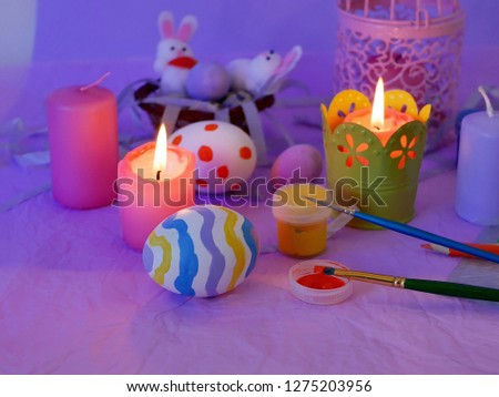 Easter decor, painted eggs, paints, brushes, lighted pink candles on a lilac background, preparation for the Easter holiday, seasonal spring celebrations