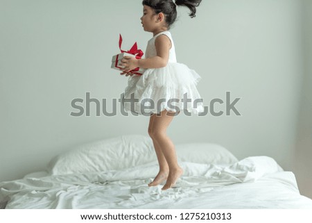 Little girl in white dress jumping on the bed having fun with your gift today. birthday party or new year.