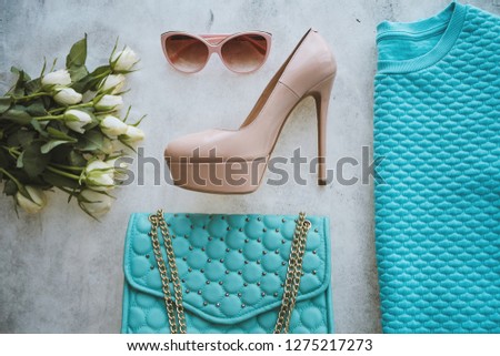 Set of fashionable clothes on the white background. Turquoise bag and sweater, beige high hills shoes, sunglasses und white roses. Trendy fashion flat lay for girls and women. Photo from above.