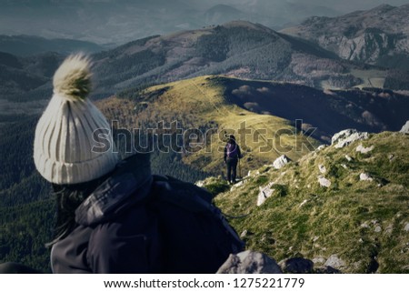 Two girls turning their backs to the camera and hiking in the mountains. girl with winter hat on the mountain.