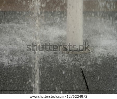 Water fountain rising up with the splashes of bubbles and droplets falling on the stone patio, background blurred and copy space.