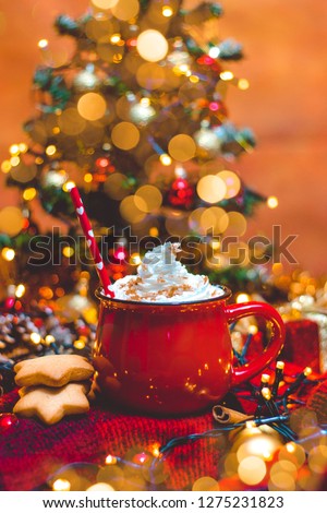 Red mug of hot coffe with Christmas lights, fresh cookies, cream, cinnamon and straw
