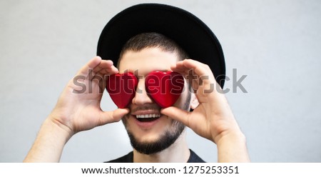 Happy bearded man holding red hearts on eyes. Valentines Day background.
