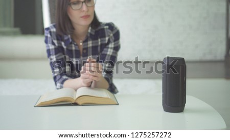 portrait beautiful woman in glasses uses voice assistant while reading a book