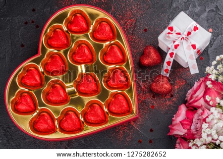 Chocolate candies in a heart shaped box, gift box, glitter red hearts and roses on dark background. Valentines day greeting card. Copy space