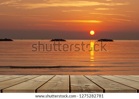 Wood planks table in the foreground and horizon over sea at sunrise in the backdrop.