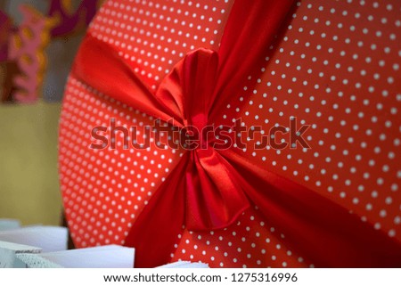 Close up of big red round box in polka dot with a ribbon and some postcards below. A red round gift-wrapped with a bow and postcards.