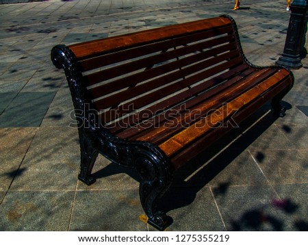 Wooden bench on masonry ground. Brown bench on metallic legs. Empty bench. Leisure in street banner template. Healthy outdoor activity. Open air leisure. Resting place for pedestrians. 