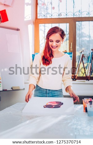 Teacher smiling. Beautiful red-haired art teacher smiling feeling satisfied with her painting